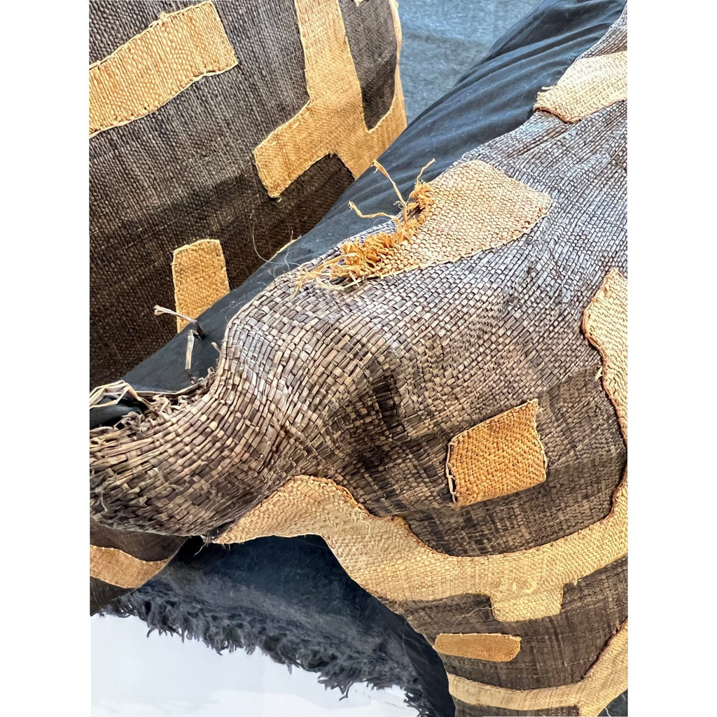 Tara Shaw African Kuba pillow featuring handwoven geometric patterns in earthy brown and tan raffia with edge wear.