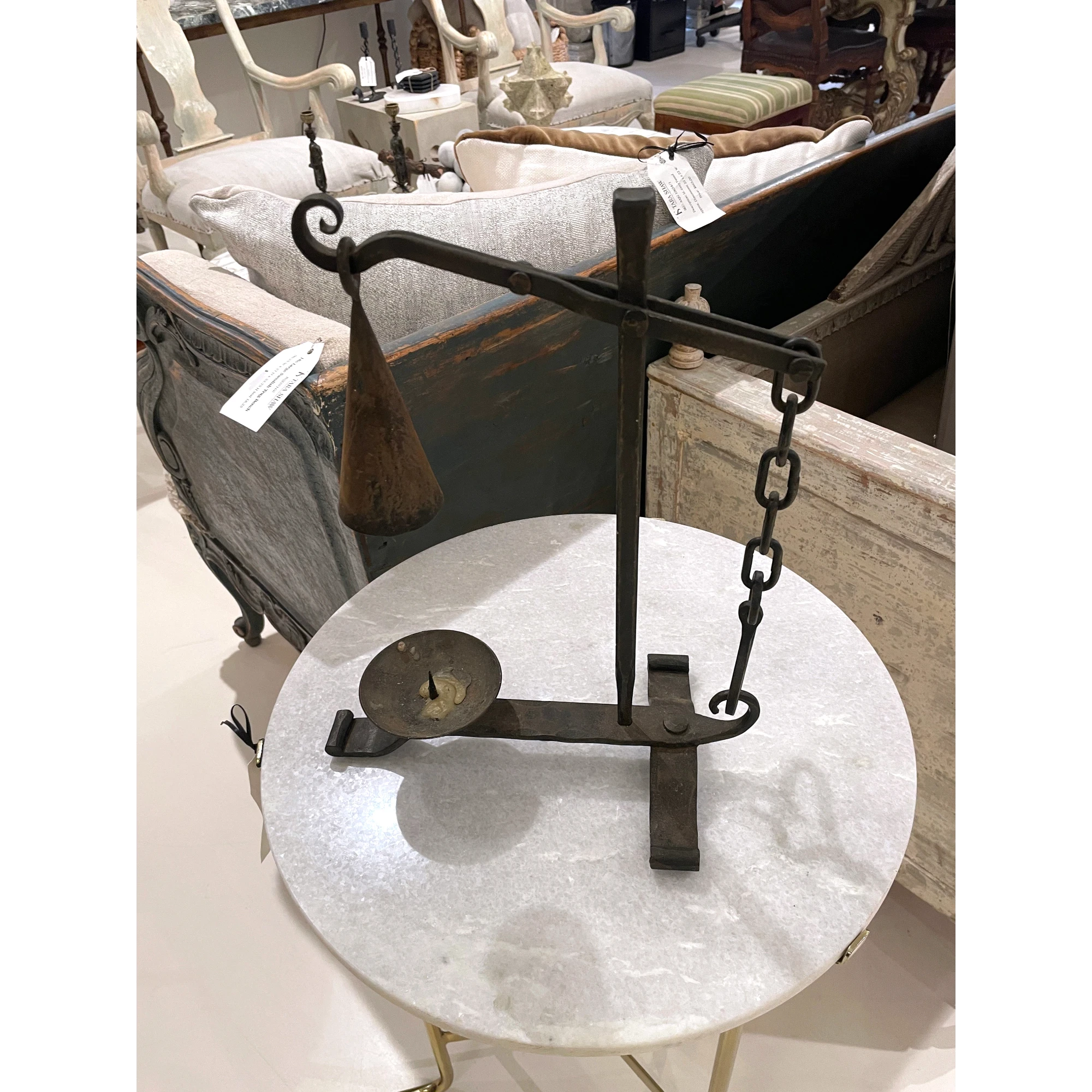 Tara Shaw 19th-century French iron candleholder with an aged patina and hanging bell detail on a marble table.