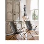 Tara Shaw pair of vintage Maison Jansen folding chairs with dark leather seats and brass-toned frames in a room.