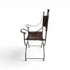 Tara Shaw early 20th century Savonarola chair with a sculptural metal frame and aged brown leather seat, side view.
