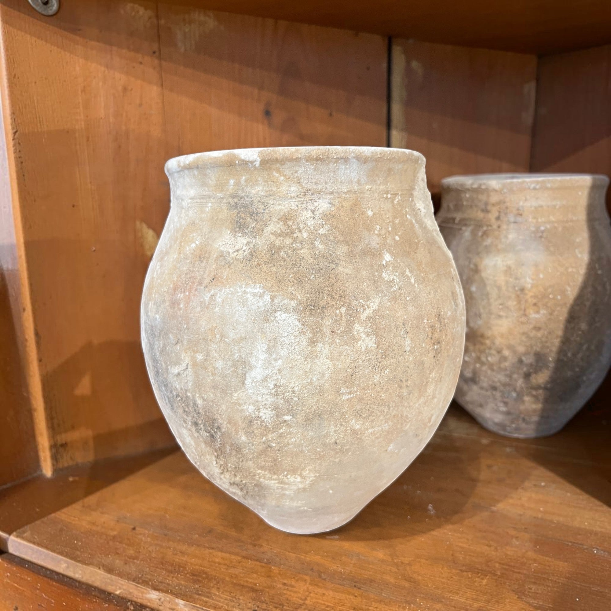 Tara Shaw rustic 18th century Spanish pottery jar with a weathered, textured patina on a wooden shelf.