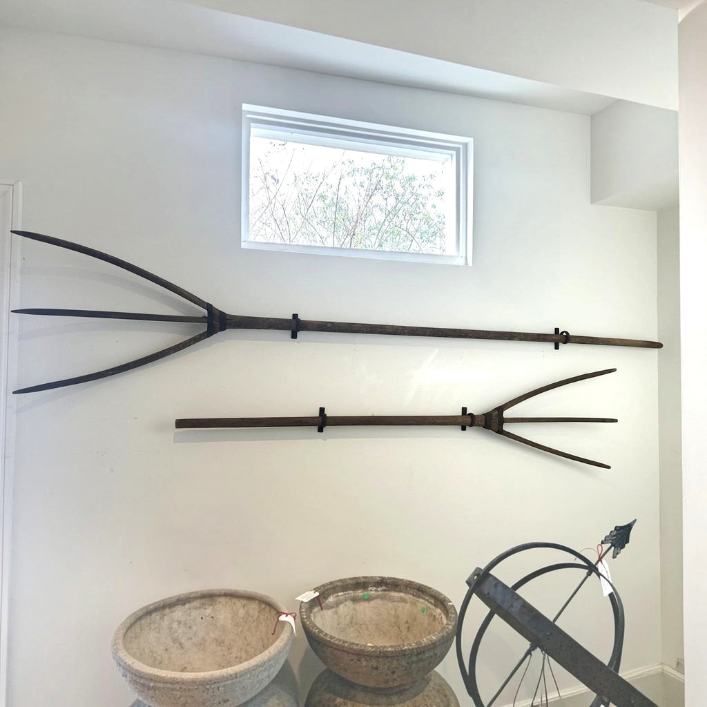 Tara Shaw vintage French pitchforks mounted on a white wall with rustic wooden handles and metal brackets